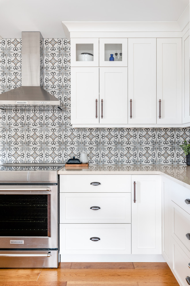 Mid-sized transitional l-shaped medium tone wood floor and brown floor kitchen pantry photo with an undermount sink, shaker cabinets, white cabinets, quartzite countertops, gray backsplash, porcelain backsplash, stainless steel appliances, an island and white countertops