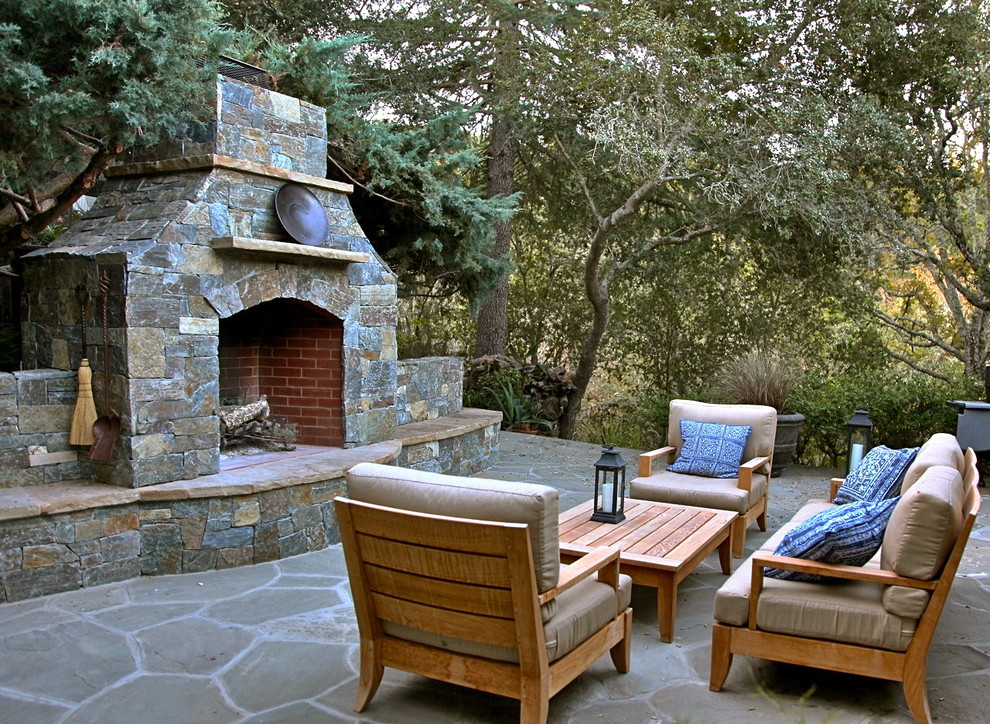 This is an example of a large country backyard patio in San Francisco with a fire feature, natural stone pavers and no cover.