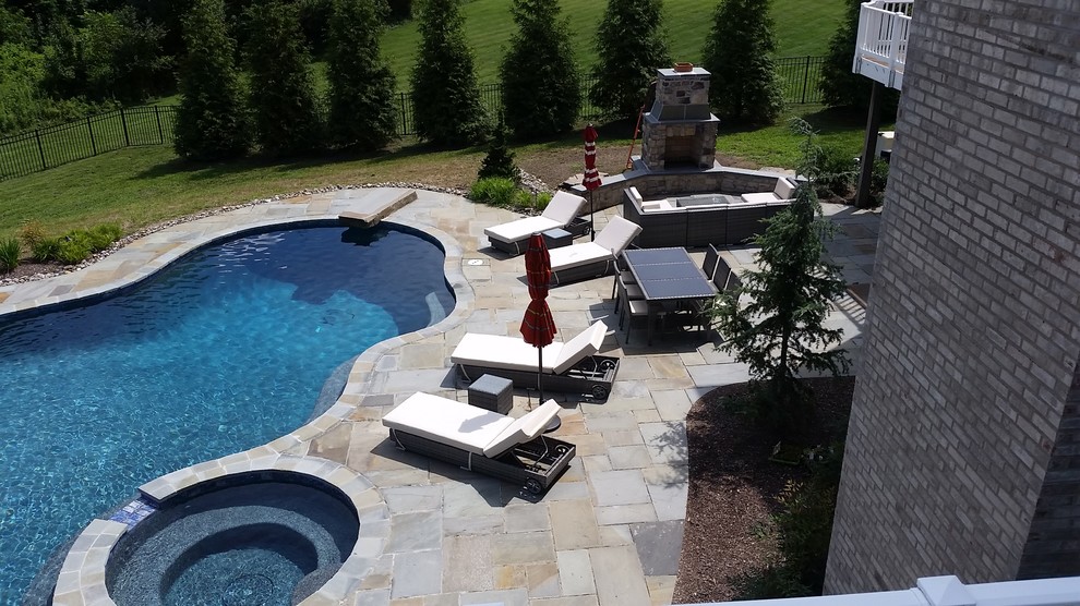 This is an example of a large traditional backyard custom-shaped natural pool in Baltimore with a hot tub and natural stone pavers.