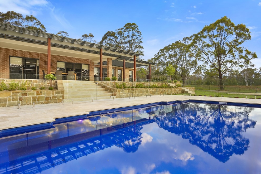 This is an example of an expansive traditional backyard rectangular lap pool in Sydney with a water feature and natural stone pavers.