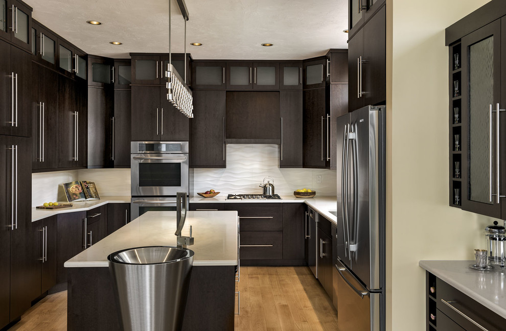 Inspiration for a mid-sized contemporary u-shaped separate kitchen in Portland Maine with flat-panel cabinets, dark wood cabinets, stainless steel appliances, with island, marble benchtops, white splashback, porcelain splashback, an undermount sink and light hardwood floors.