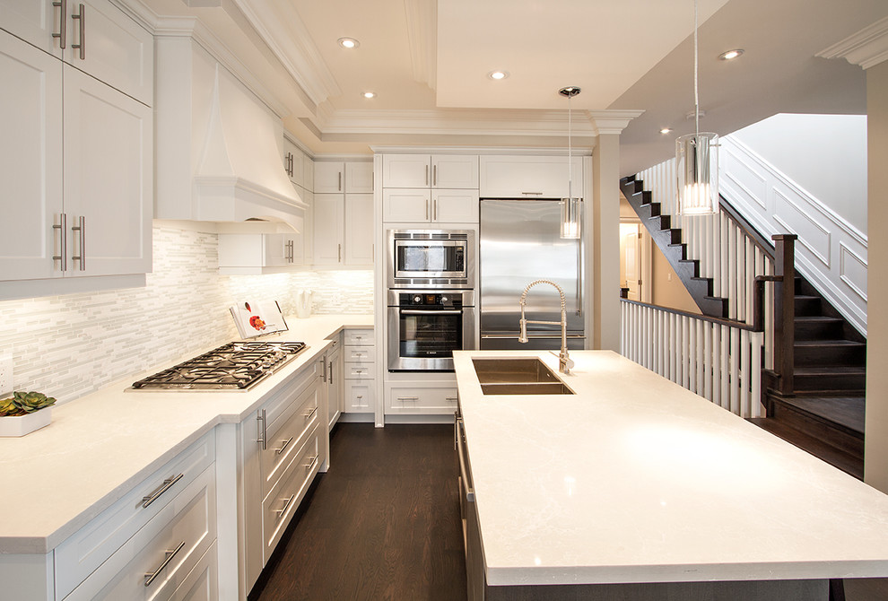 Photo of a mid-sized transitional u-shaped eat-in kitchen in Toronto with shaker cabinets, white splashback, dark hardwood floors, an undermount sink, stainless steel appliances, with island, light wood cabinets, mosaic tile splashback, brown floor and white benchtop.