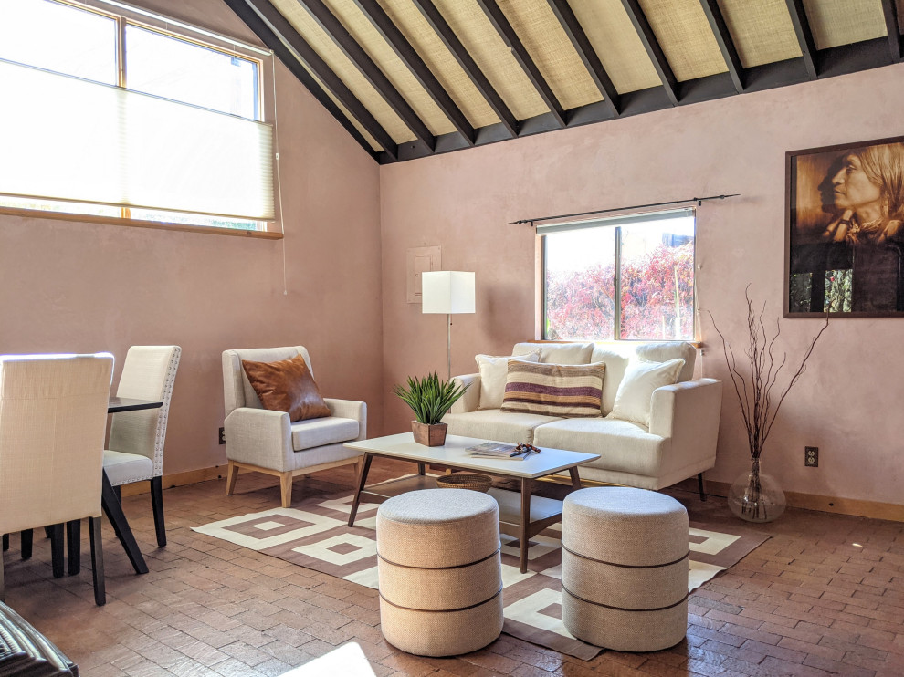 Foto de salón abierto de estilo americano pequeño sin televisor con paredes rosas, suelo de ladrillo, estufa de leña, marco de chimenea de yeso, suelo marrón y vigas vistas