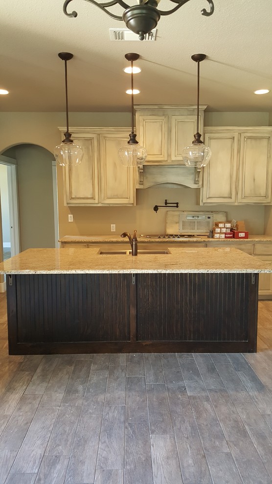 Inspiration for a mid-sized traditional l-shaped open plan kitchen in Austin with a farmhouse sink, raised-panel cabinets, white cabinets, granite benchtops, stainless steel appliances, medium hardwood floors, with island and brown floor.