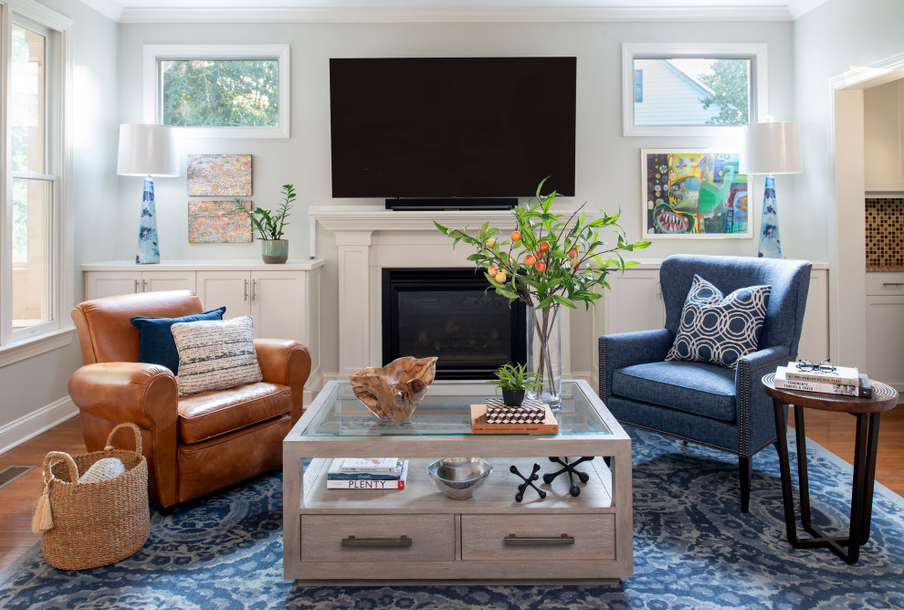Photo of a mid-sized transitional open concept living room in Raleigh with grey walls, medium hardwood floors, a standard fireplace, a wood fireplace surround, a wall-mounted tv and brown floor.