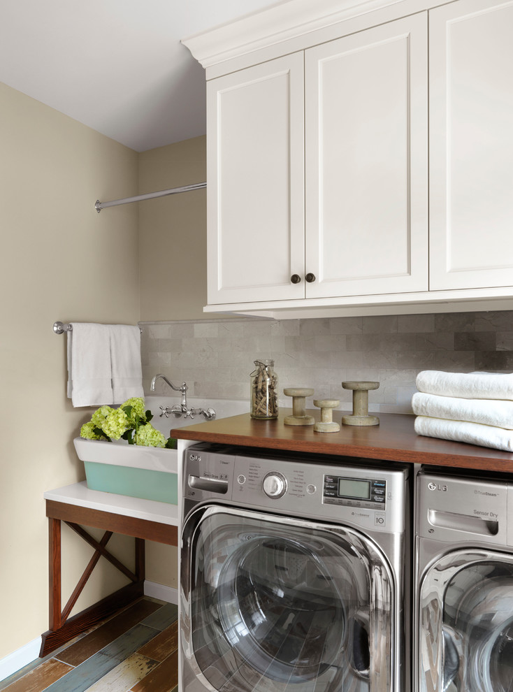 Inspiration for a country single-wall dedicated laundry room in St Louis with a farmhouse sink, shaker cabinets, white cabinets, wood benchtops, beige walls, painted wood floors, a side-by-side washer and dryer, multi-coloured floor and brown benchtop.