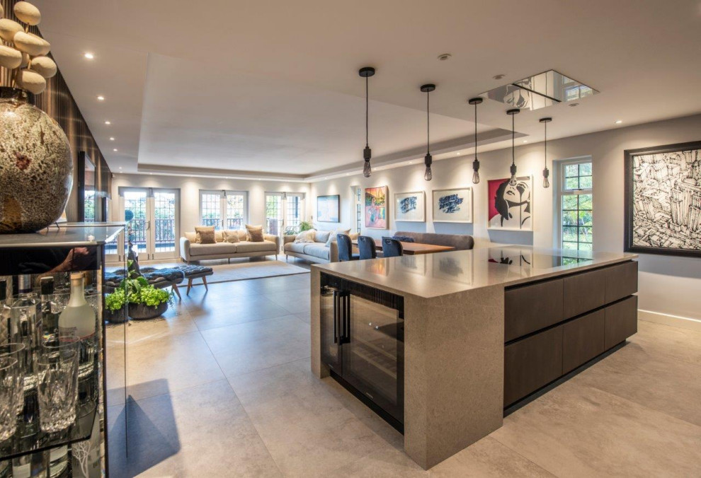 Inspiration for a large contemporary galley porcelain tile, gray floor and coffered ceiling open concept kitchen remodel in Manchester with an undermount sink, flat-panel cabinets, gray cabinets, quartzite countertops, beige backsplash, stone slab backsplash, black appliances, an island and beige countertops