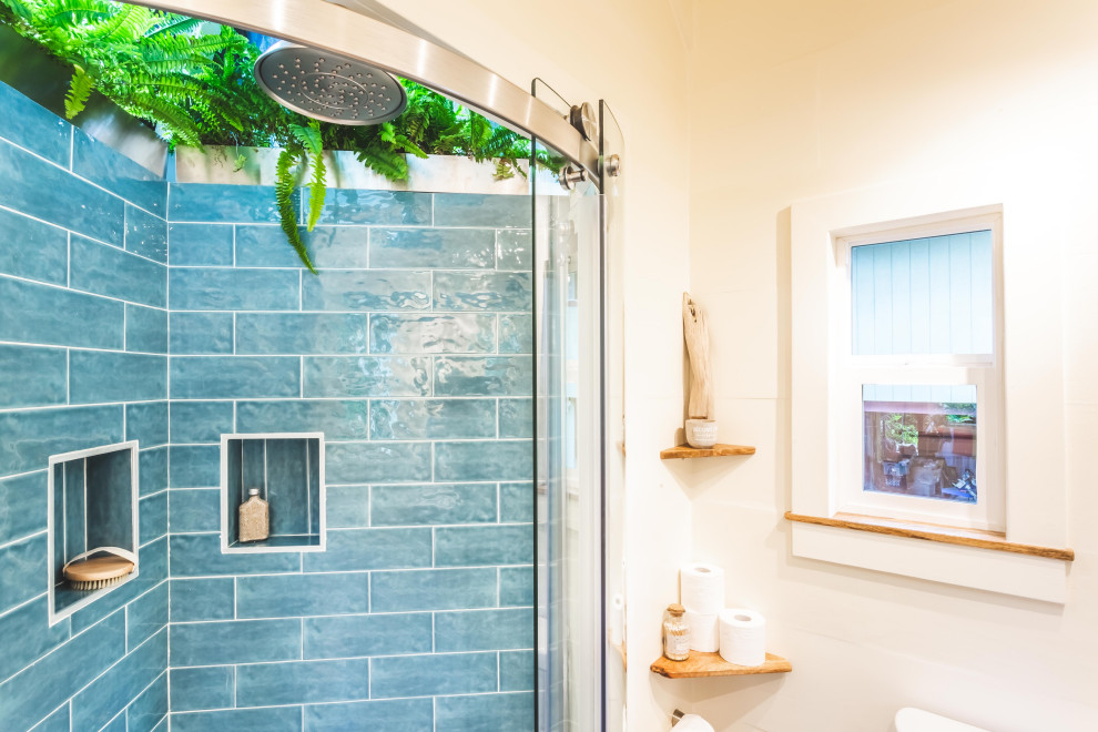 Photo of a small beach style 3/4 bathroom in Hawaii with open cabinets, light wood cabinets, a corner shower, a two-piece toilet, blue tile, ceramic tile, white walls, laminate floors, a vessel sink, wood benchtops, brown floor, a sliding shower screen, brown benchtops, a niche, a single vanity, a floating vanity and vaulted.