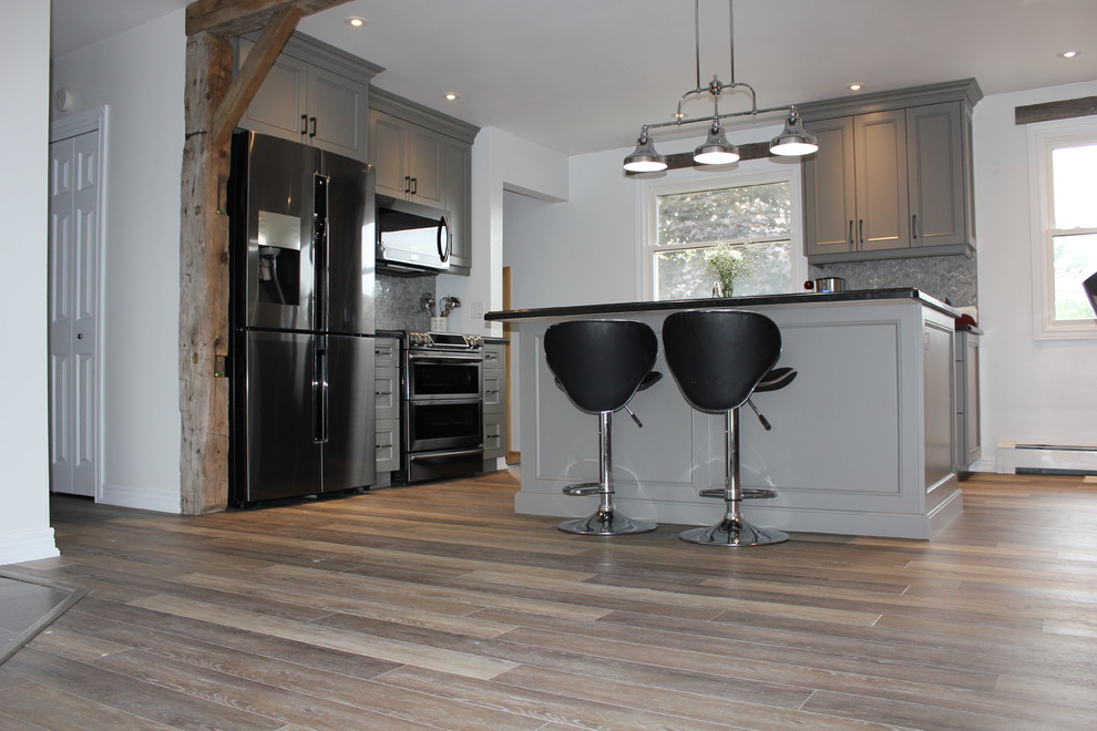Photo of a mid-sized transitional l-shaped open plan kitchen in Toronto with beaded inset cabinets, grey cabinets, mosaic tile splashback, black appliances, vinyl floors, with island, beige floor, an undermount sink and grey splashback.