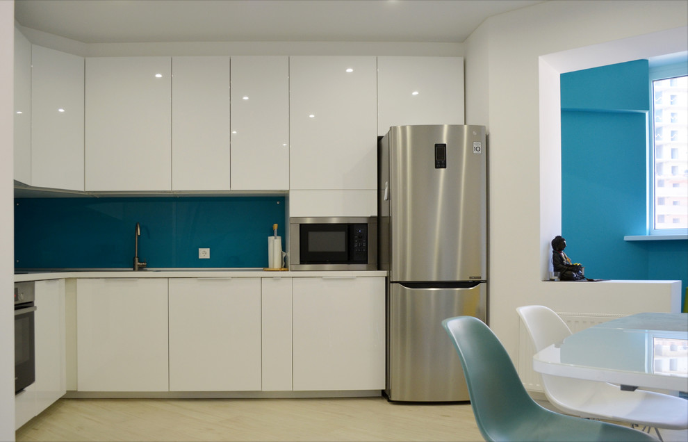 Пример оригинального дизайна: угловая кухня среднего размера с белыми фасадами, синим фартуком и фартуком из стекла