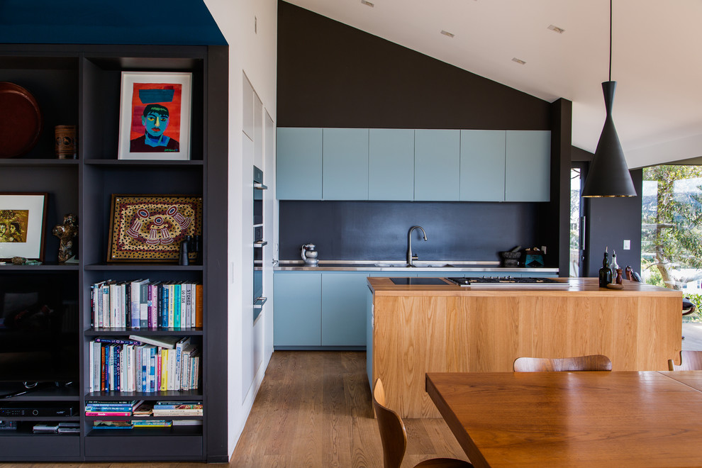 Contemporary galley open plan kitchen in Wellington with flat-panel cabinets, blue cabinets, black splashback, dark hardwood floors and with island.