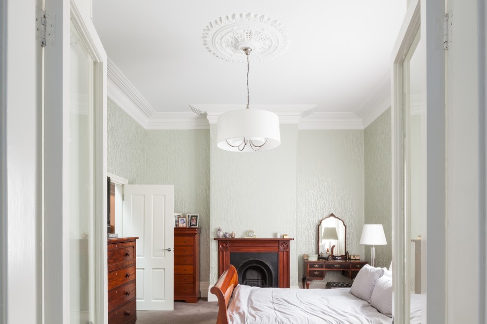 This is an example of a large traditional master bedroom in Sydney with green walls, carpet, a standard fireplace and a wood fireplace surround.