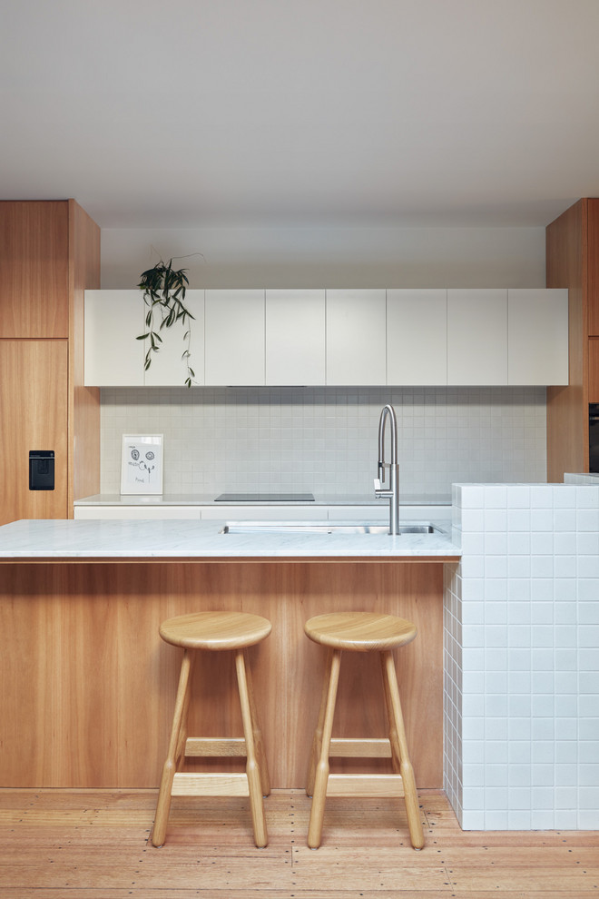 This is an example of a scandinavian kitchen in Melbourne with an undermount sink, flat-panel cabinets, white cabinets, white splashback, light hardwood floors and white benchtop.