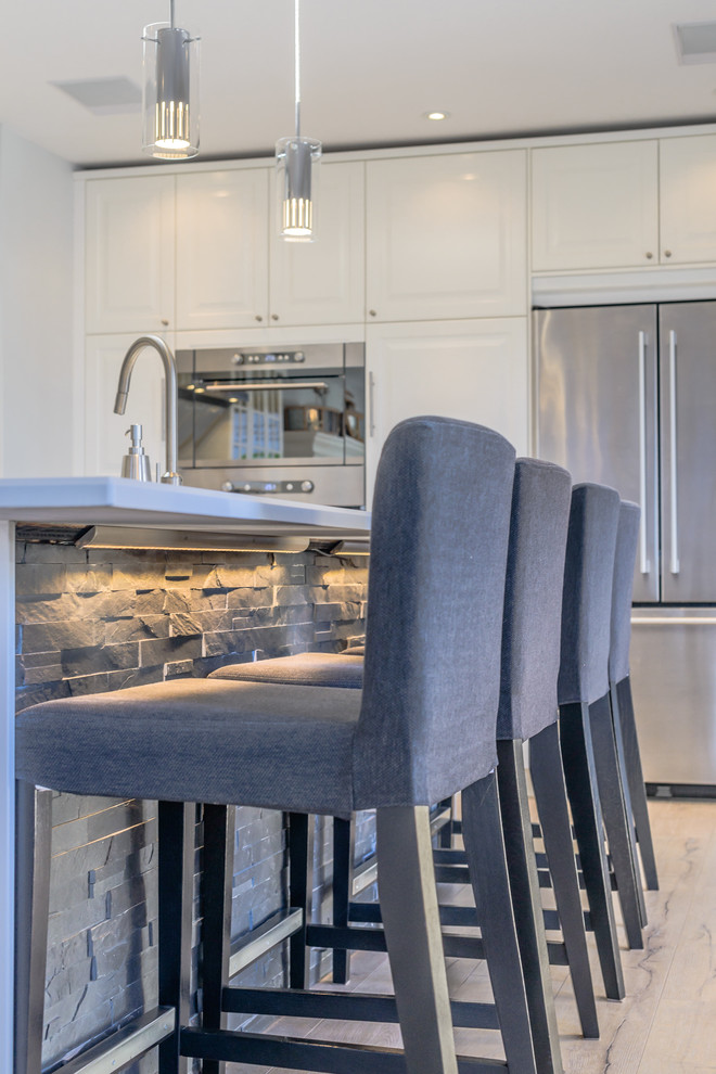 Photo of an expansive beach style galley open plan kitchen in Toronto with a double-bowl sink, beaded inset cabinets, white cabinets, laminate benchtops, grey splashback, stone tile splashback, stainless steel appliances, light hardwood floors and with island.