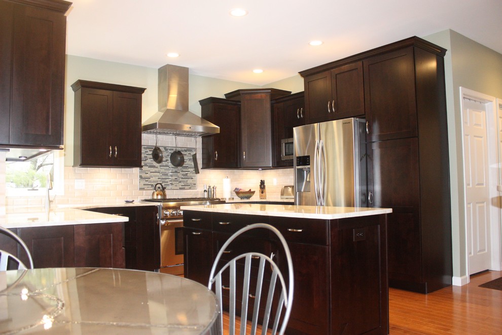 Example of a mid-sized transitional u-shaped medium tone wood floor kitchen design with shaker cabinets, dark wood cabinets, white backsplash, stainless steel appliances and an island