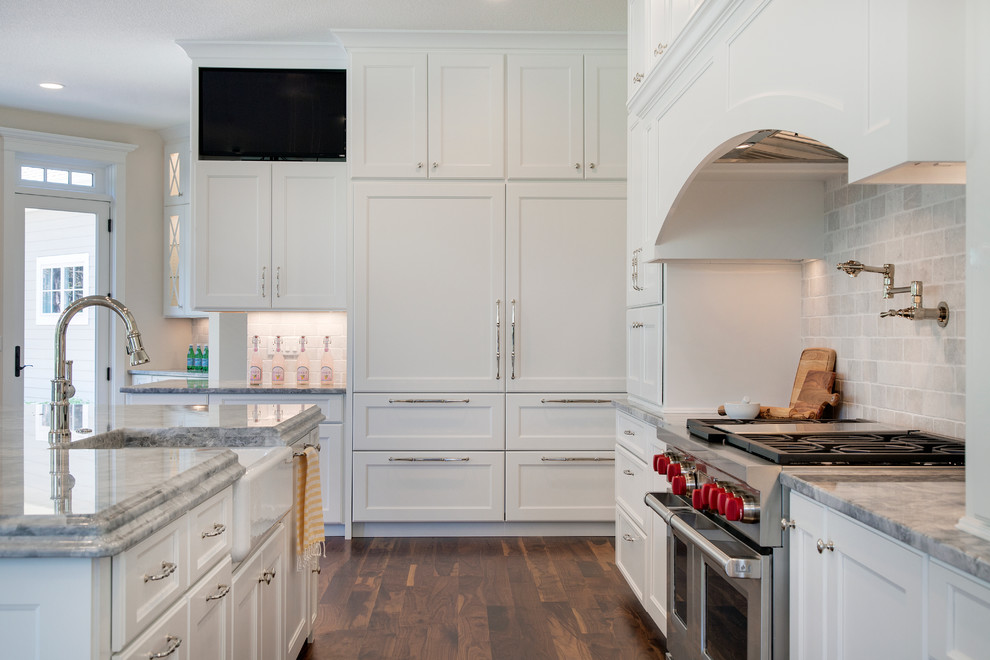 Inspiration for an expansive traditional u-shaped open plan kitchen in Minneapolis with a farmhouse sink, recessed-panel cabinets, white cabinets, marble benchtops, white splashback, stone tile splashback, stainless steel appliances, medium hardwood floors and with island.