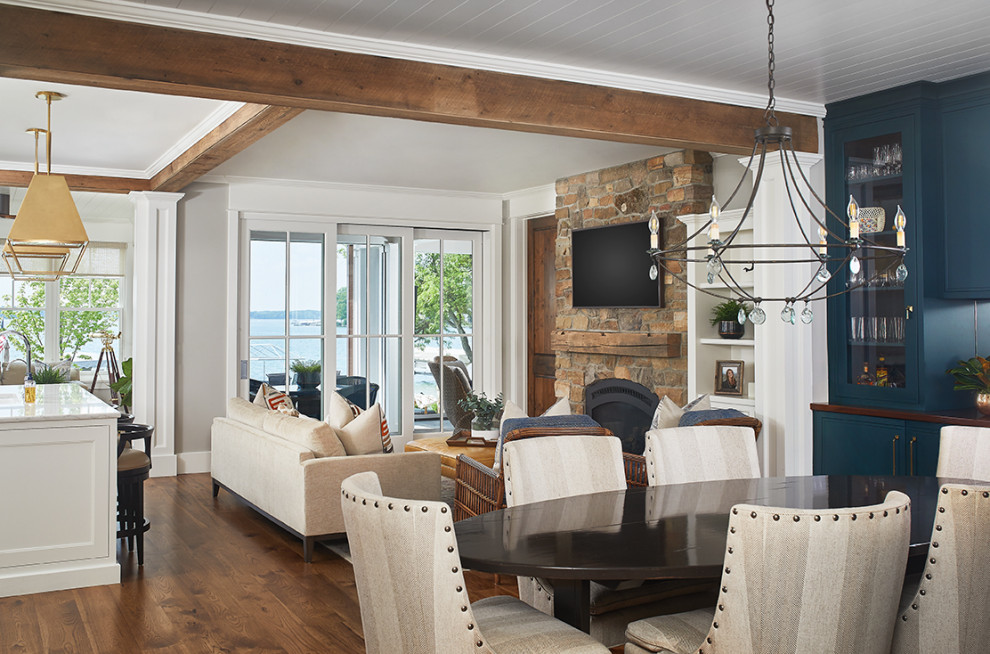 Design ideas for a mid-sized beach style open plan dining in Grand Rapids with grey walls, medium hardwood floors, a standard fireplace, a stone fireplace surround and brown floor.