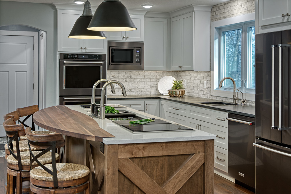 Design ideas for a mid-sized transitional l-shaped eat-in kitchen in Minneapolis with an undermount sink, flat-panel cabinets, white cabinets, soapstone benchtops, white splashback, brick splashback, black appliances, dark hardwood floors, with island, brown floor and white benchtop.