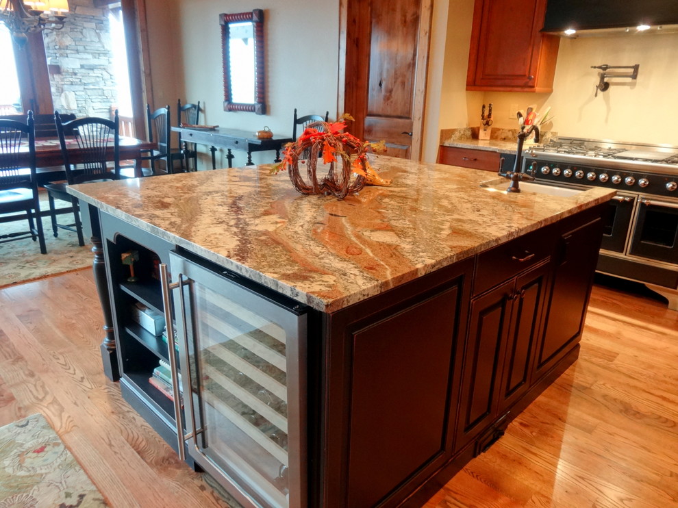 Photo of a large country u-shaped eat-in kitchen in Charlotte with a farmhouse sink, raised-panel cabinets, dark wood cabinets, granite benchtops, beige splashback, stainless steel appliances, light hardwood floors and with island.