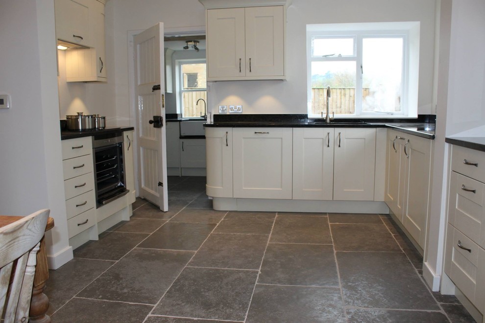 Design ideas for a large country eat-in kitchen in Dorset with a drop-in sink, shaker cabinets, beige cabinets, granite benchtops, black splashback, coloured appliances, limestone floors and with island.