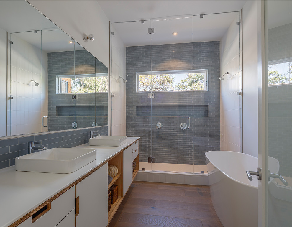 Inspiration for a large midcentury master bathroom in San Francisco with furniture-like cabinets, white cabinets, a freestanding tub, an alcove shower, a two-piece toilet, blue tile, subway tile, white walls, medium hardwood floors, a vessel sink, solid surface benchtops, brown floor and a hinged shower door.
