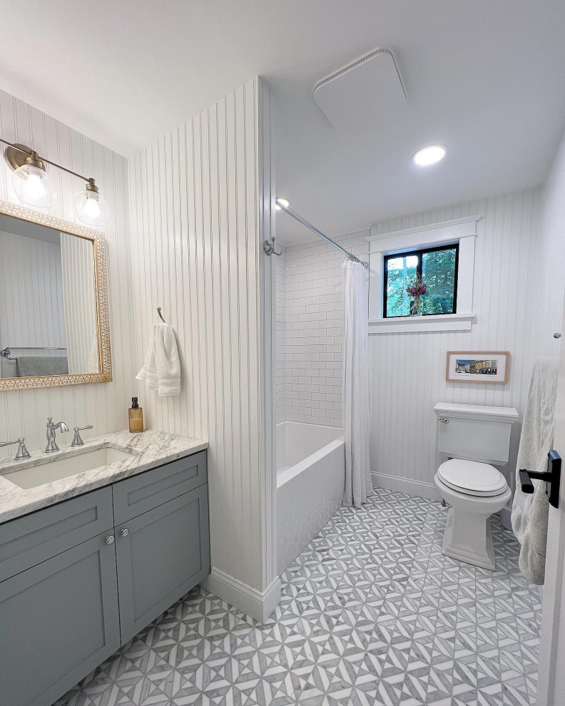 Photo of a mid-sized traditional bathroom in Boston with shaker cabinets, blue cabinets, a shower/bathtub combo, white tile, subway tile, white walls, marble floors, marble benchtops, a shower curtain, a single vanity, a built-in vanity and decorative wall panelling.