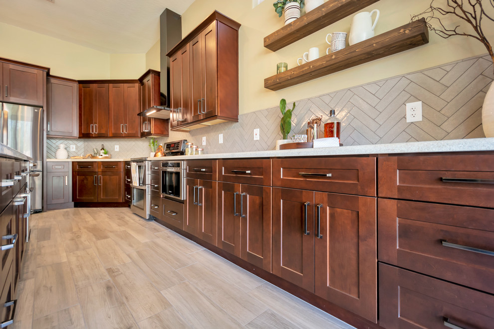 Mid-sized transitional l-shaped porcelain tile and brown floor open concept kitchen photo in Phoenix with a single-bowl sink, shaker cabinets, brown cabinets, granite countertops, gray backsplash, brick backsplash, stainless steel appliances, an island and multicolored countertops