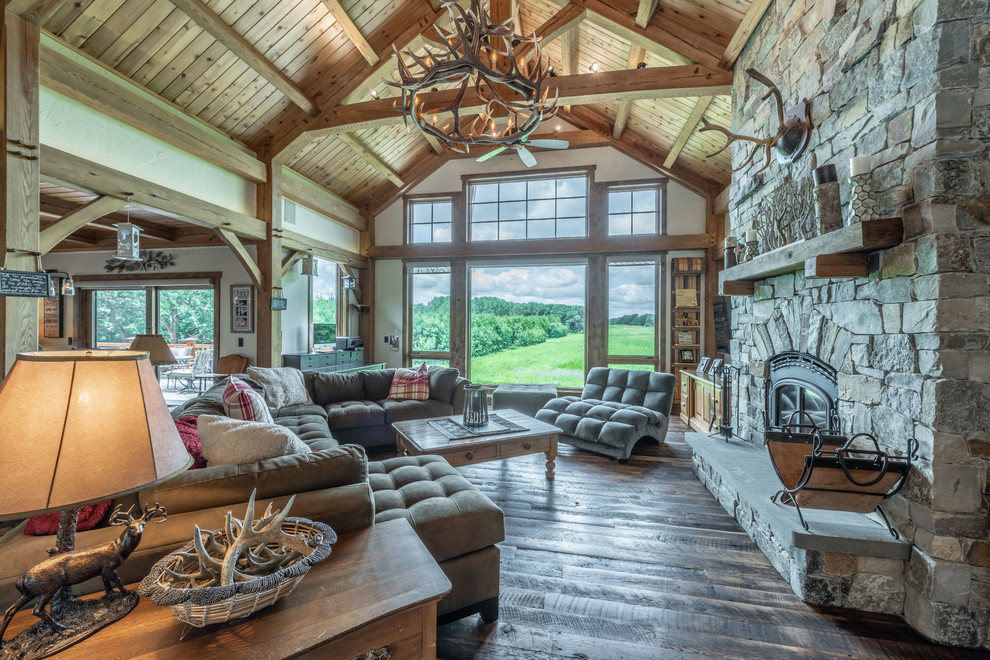 This is an example of a large country open concept living room in Milwaukee with beige walls, dark hardwood floors, a standard fireplace, a stone fireplace surround, a built-in media wall and brown floor.