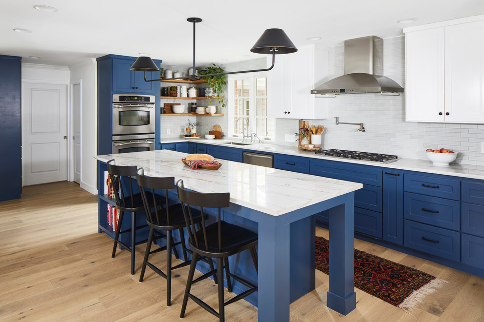 Large transitional l-shaped light wood floor and beige floor open concept kitchen photo in Austin with an undermount sink, shaker cabinets, blue cabinets, marble countertops, white backsplash, subway tile backsplash, stainless steel appliances and an island