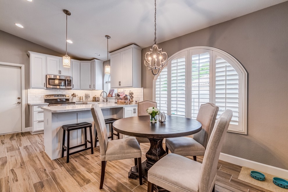 Example of a mid-sized transitional u-shaped porcelain tile and beige floor eat-in kitchen design in Phoenix with a farmhouse sink, shaker cabinets, white cabinets, quartz countertops, white backsplash, subway tile backsplash, stainless steel appliances and white countertops