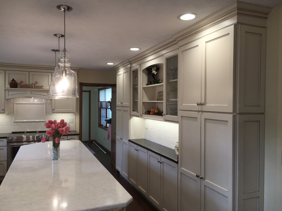Example of a large transitional medium tone wood floor and brown floor eat-in kitchen design with an undermount sink, flat-panel cabinets, white cabinets, granite countertops, white backsplash, porcelain backsplash, stainless steel appliances and an island
