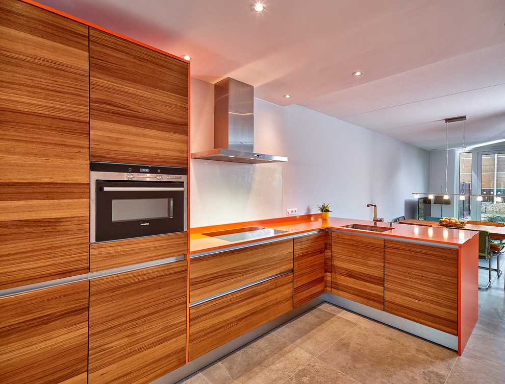 Large contemporary l-shaped eat-in kitchen in Other with an undermount sink, flat-panel cabinets, medium wood cabinets, glass sheet splashback, stainless steel appliances, solid surface benchtops, white splashback, a peninsula, concrete floors and orange benchtop.