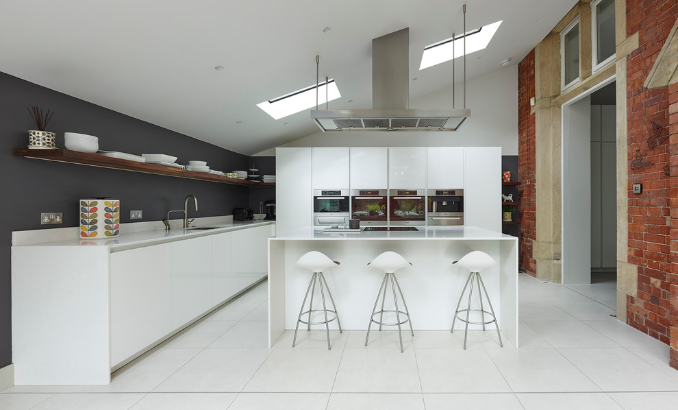 Large industrial l-shaped open plan kitchen in Other with flat-panel cabinets, white cabinets, quartzite benchtops, stainless steel appliances, porcelain floors, with island, a drop-in sink, white floor, grey splashback and white benchtop.