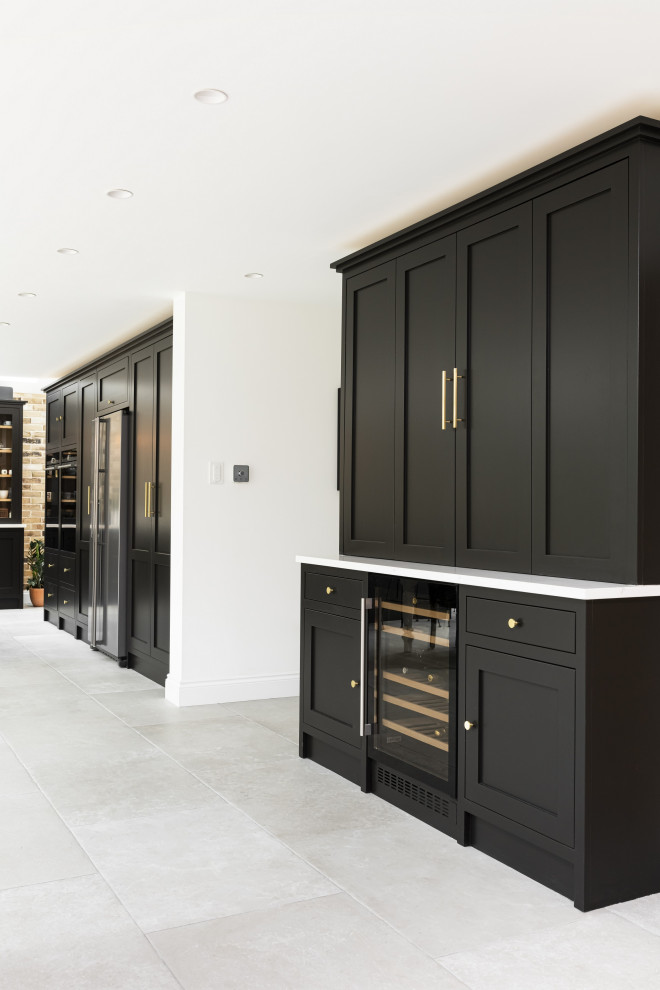 Design ideas for a large traditional single-wall kitchen/diner in London with a belfast sink, shaker cabinets, black cabinets, quartz worktops, black appliances, porcelain flooring, an island, grey floors, white worktops and a feature wall.