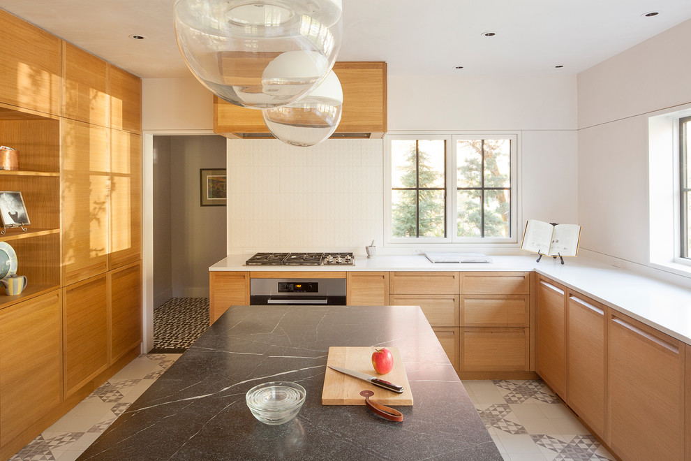 Photo of a contemporary u-shaped kitchen in Portland with flat-panel cabinets, medium wood cabinets, white splashback, stainless steel appliances, with island, multi-coloured floor and white benchtop.