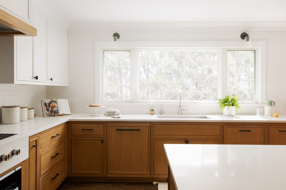 Design ideas for a mid-sized transitional l-shaped eat-in kitchen in New York with a drop-in sink, beaded inset cabinets, white cabinets, solid surface benchtops, white splashback, porcelain splashback, stainless steel appliances, medium hardwood floors, with island and white benchtop.