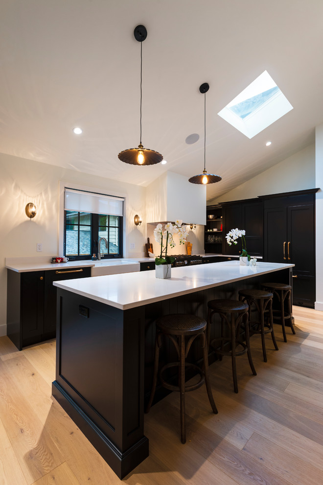 Inspiration for a mid-sized rustic l-shaped light wood floor and beige floor open concept kitchen remodel in Vancouver with a farmhouse sink, shaker cabinets, black cabinets, quartz countertops, paneled appliances, an island and white countertops