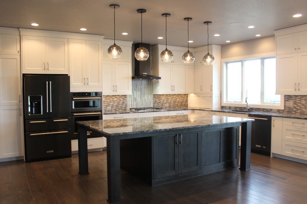 Example of a large transitional l-shaped medium tone wood floor and brown floor kitchen design with an undermount sink, shaker cabinets, white cabinets, granite countertops, multicolored backsplash, mosaic tile backsplash, black appliances and an island