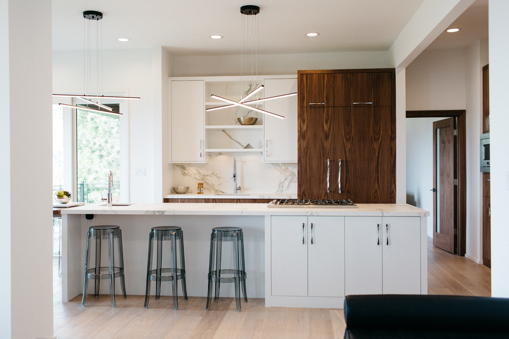 Photo of a mid-sized contemporary galley open plan kitchen in Seattle with an undermount sink, flat-panel cabinets, white cabinets, white splashback, panelled appliances, medium hardwood floors, with island, marble benchtops and stone slab splashback.