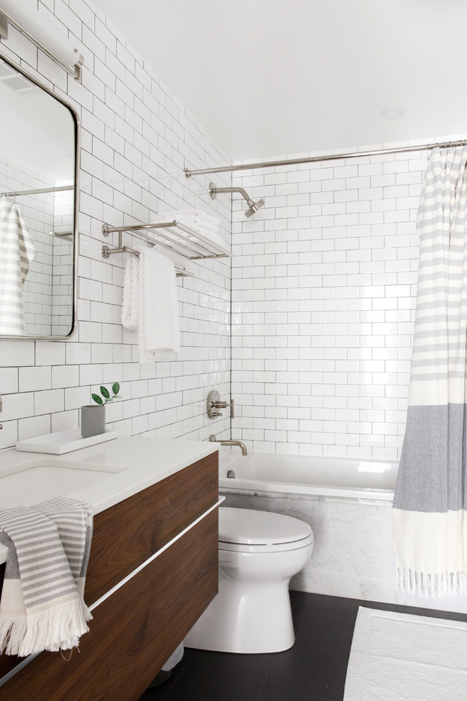 Photo of a mid-sized scandinavian bathroom in Toronto with a shower/bathtub combo, a drop-in sink, flat-panel cabinets, dark wood cabinets, a drop-in tub, white tile, subway tile, white walls, black floor, a shower curtain, white benchtops, marble benchtops and a one-piece toilet.