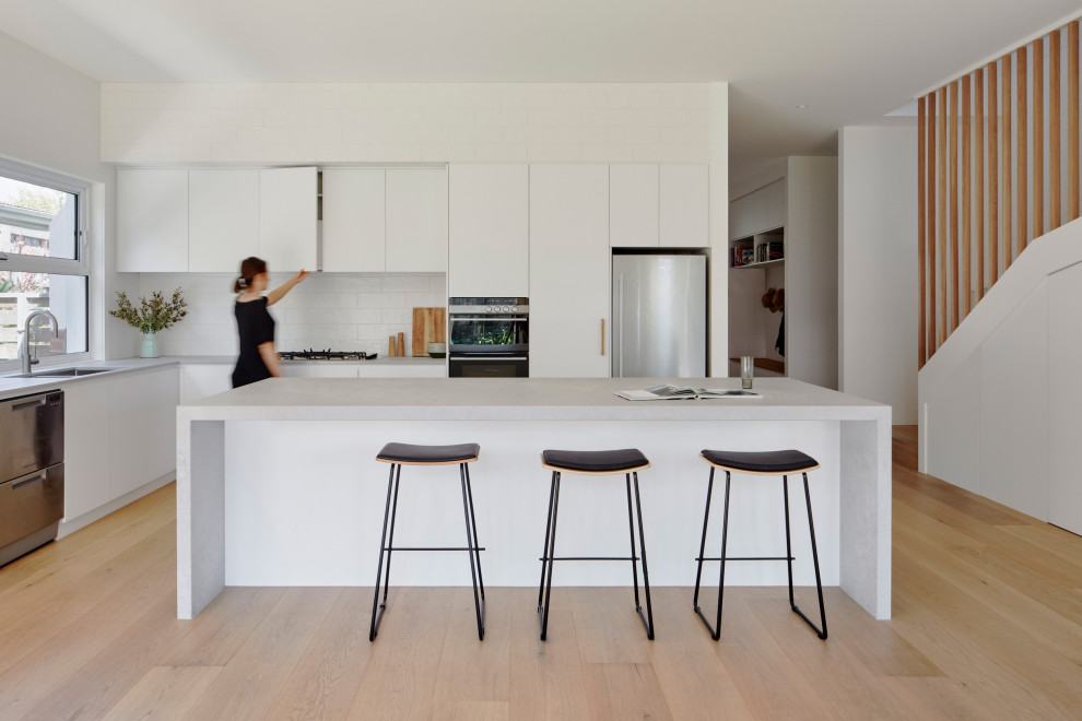 Inspiration for a mid-sized modern galley eat-in kitchen in Melbourne with a drop-in sink, quartz benchtops, white splashback, ceramic splashback, stainless steel appliances, light hardwood floors, with island and grey benchtop.
