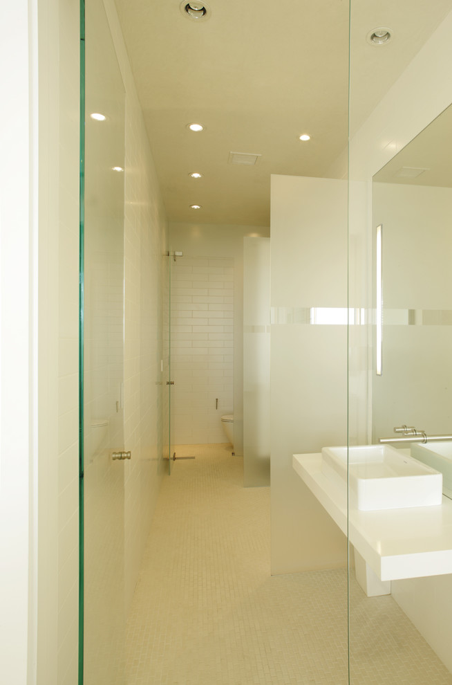 This is an example of a large contemporary master bathroom in Orange County with a freestanding tub, an alcove shower, a hinged shower door, a one-piece toilet, white walls, porcelain floors, a wall-mount sink, solid surface benchtops and beige floor.