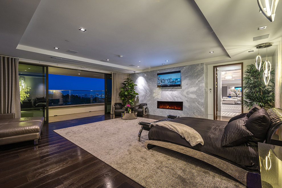 This is an example of a large modern guest bedroom in Los Angeles with grey walls, dark hardwood floors, a hanging fireplace, a stone fireplace surround, brown floor and recessed.