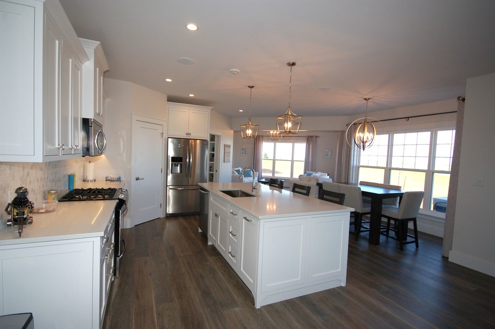 Example of a mid-sized transitional l-shaped dark wood floor and brown floor open concept kitchen design with a single-bowl sink, shaker cabinets, white cabinets, solid surface countertops, white backsplash, stone tile backsplash and an island