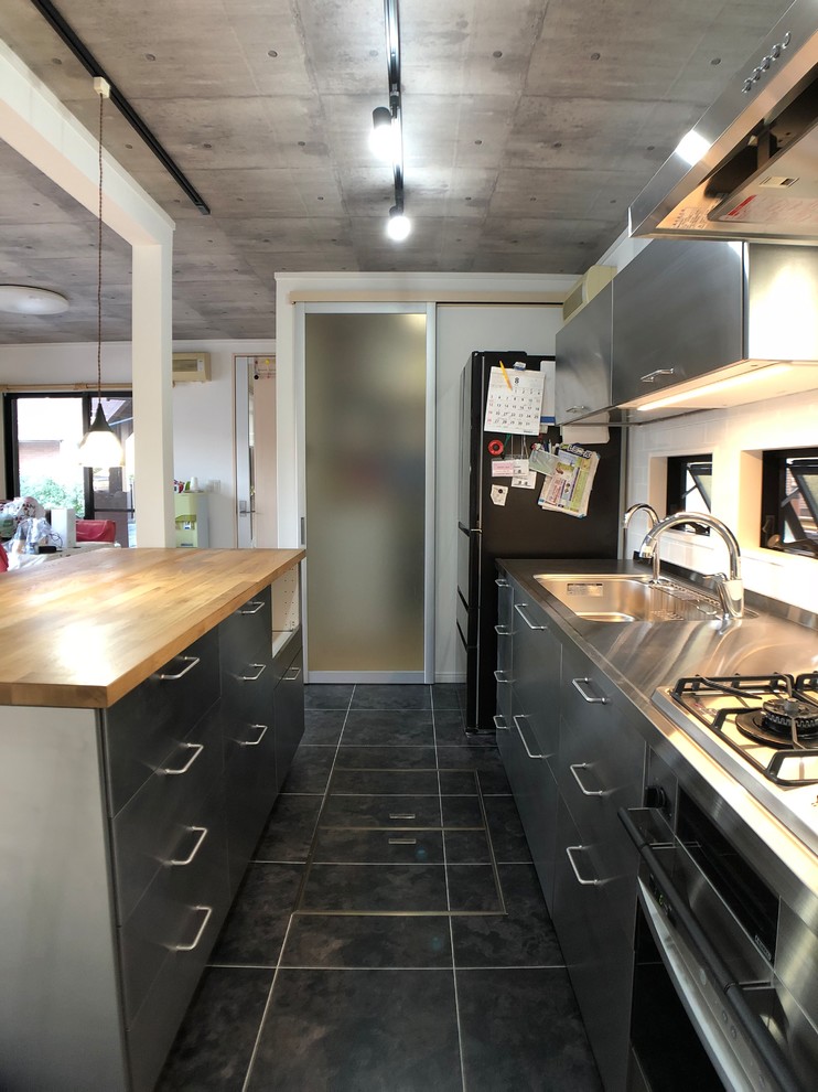 Industrial single-wall kitchen in Other with an integrated sink, flat-panel cabinets, stainless steel cabinets, stainless steel benchtops, with island, black floor and brown benchtop.