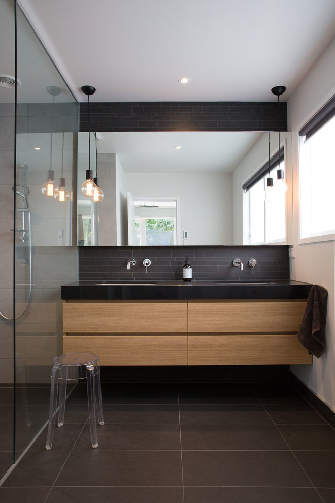 This is an example of a contemporary bathroom in Auckland with flat-panel cabinets, brown cabinets, black tile, white walls, an integrated sink, wood benchtops, black floor and a hinged shower door.