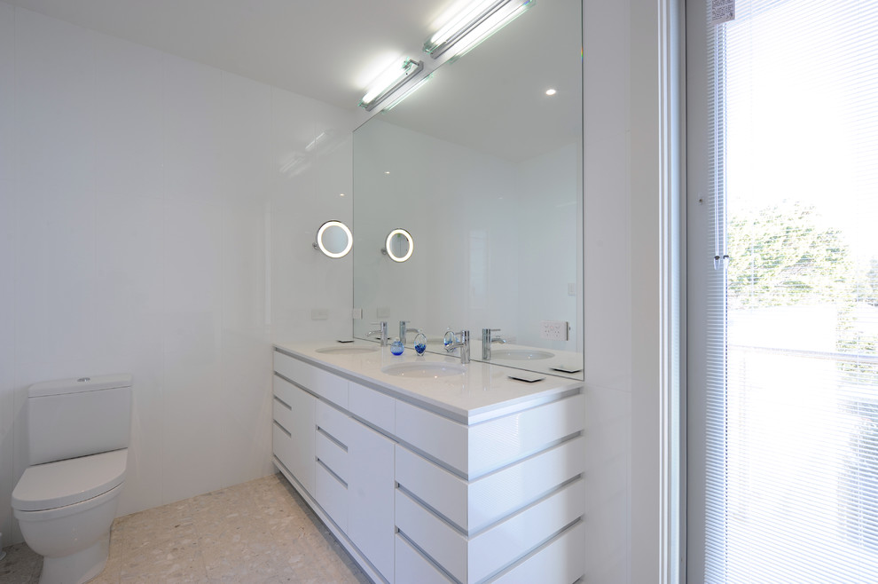 Mid-sized beach style master bathroom in Adelaide with flat-panel cabinets, white cabinets, solid surface benchtops, white tile and ceramic floors.