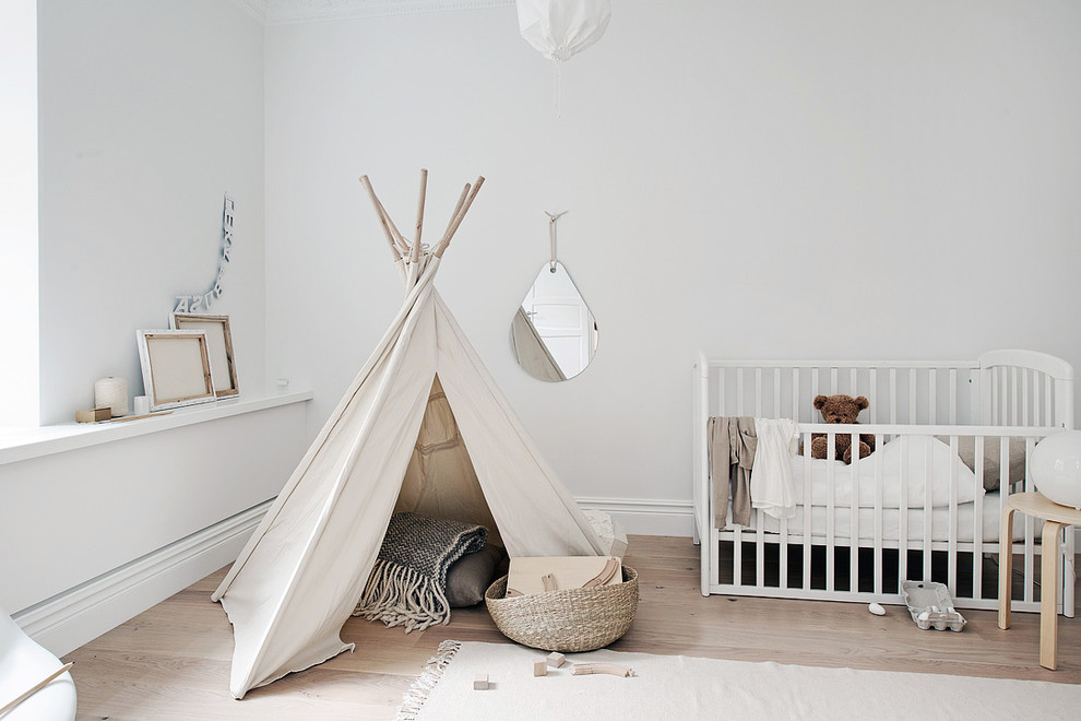 Photo of a mid-sized scandinavian gender-neutral nursery in Gothenburg with white walls, light hardwood floors and beige floor.