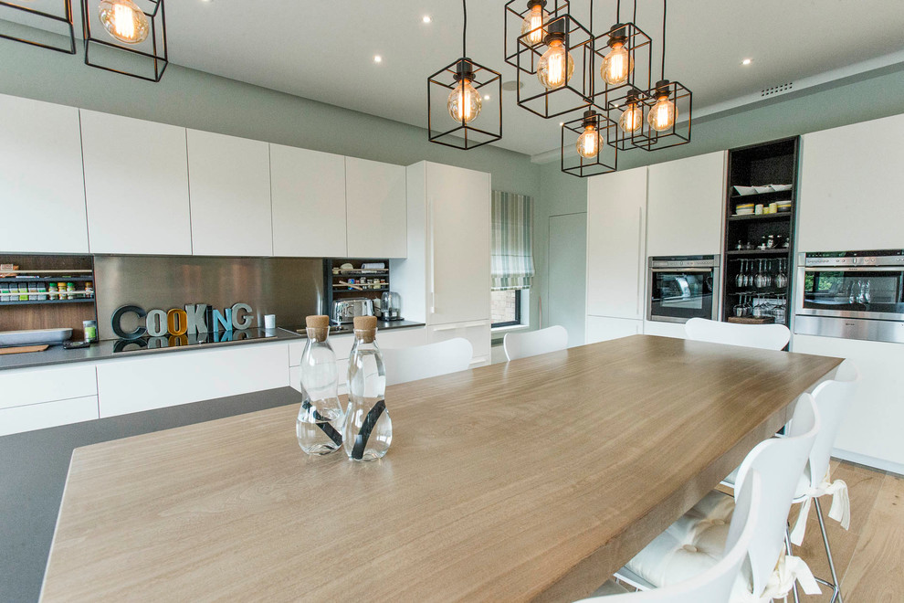 Cette image montre cuisine américaine in U With un évier 2 bacs, des portes de placard blanches, un plan de travail en quartz modifié, une crédence grise, une crédence en quartz modifié, un électroménager en acier inoxydable, îlot, un sol marron, un plan de travail gris and parquet clair.