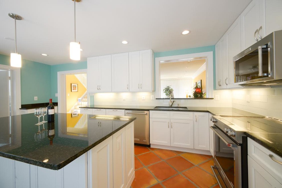 Mid-sized transitional l-shaped separate kitchen in DC Metro with an undermount sink, shaker cabinets, white cabinets, granite benchtops, white splashback, glass tile splashback, stainless steel appliances, terra-cotta floors, with island and brown floor.